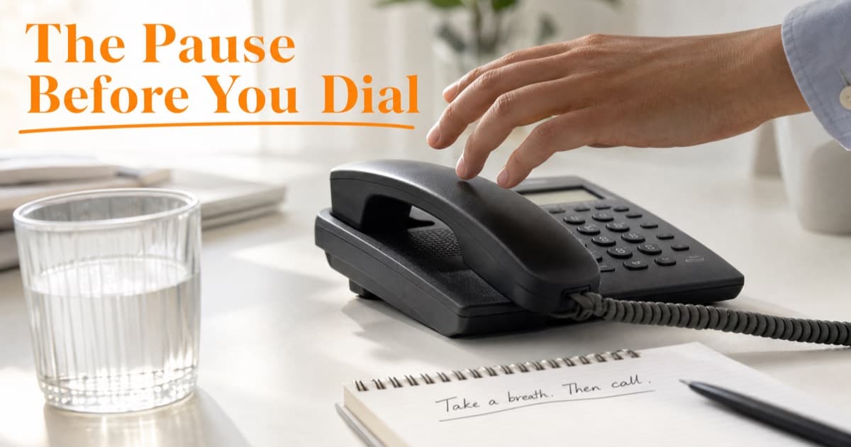 A hand hovering just above a desk phone receiver, beside a glass of water and a notepad reading 'Take a breath. Then call.'
