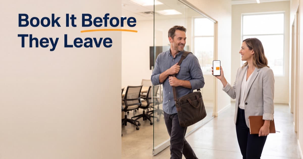 Two people walking out of a bright glass-walled meeting room, one holding up a phone with a calendar on screen to book the next meeting before the other leaves, next to the words Book It Before They Leave