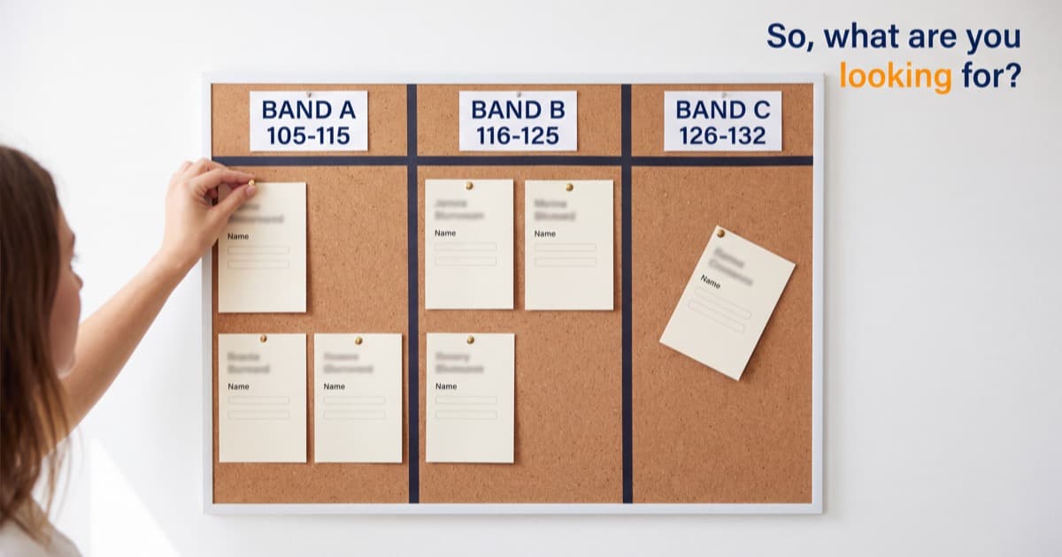 A pinboard on a bright office wall holding candidate cards slotted into three labelled pay bands, a hand pinning one card into the lowest column, with the line So, what are you looking for? set in navy and orange on the wall beside it